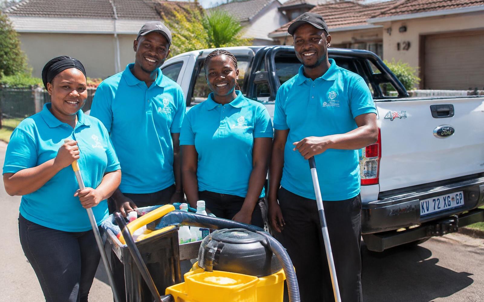 Four team members in blue uniforms standing beside a bakkie with cleaning equipment